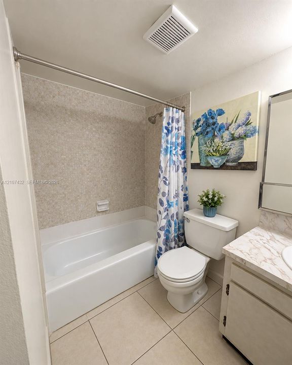 Bathroom featuring a porcelain bathtub with stone-patterned surround, tiled flooring, and a vanity topped with a stone-finish countertop