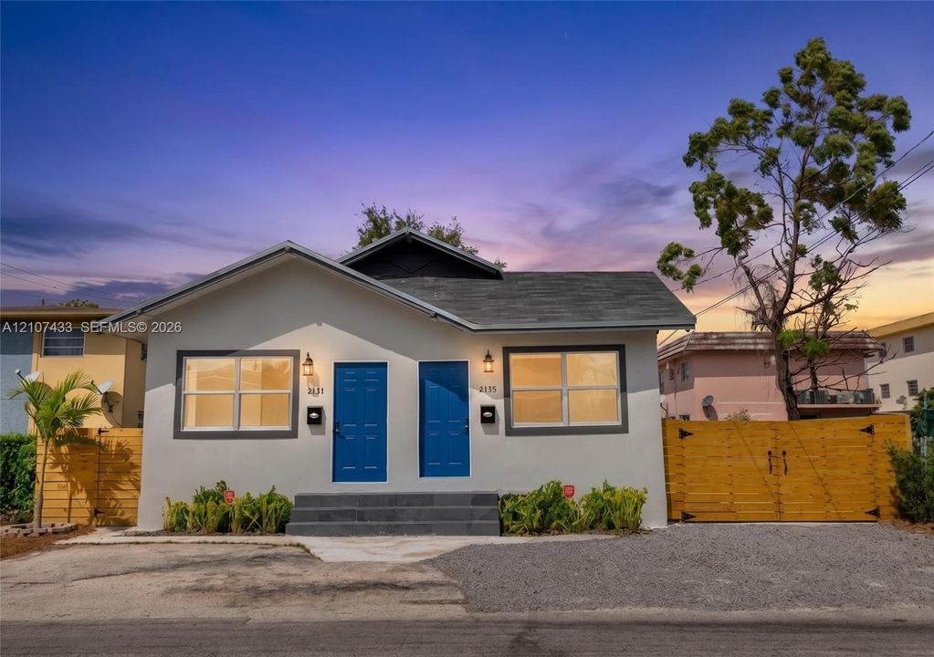 Exterior view featuring light-toned stucco siding, two vibrant blue entry doors, a multi-step concrete stoop, and natural wood-finish privacy fencing