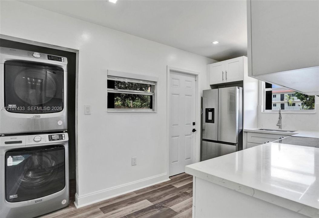 Kitchen featuring stainless steel appliances, stacked laundry unit, white cabinetry, solid-surface countertops, and wood-finish flooring