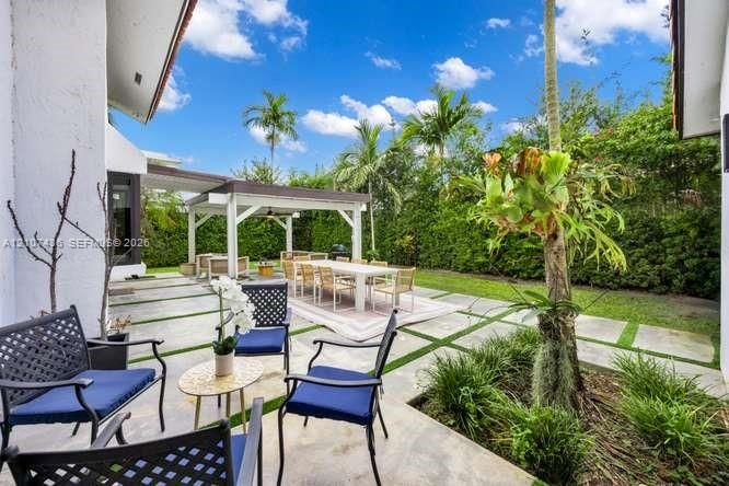 Spacious outdoor living area featuring a paved patio with geometric grass inlay, a custom wood-framed pergola, and mature perimeter landscaping