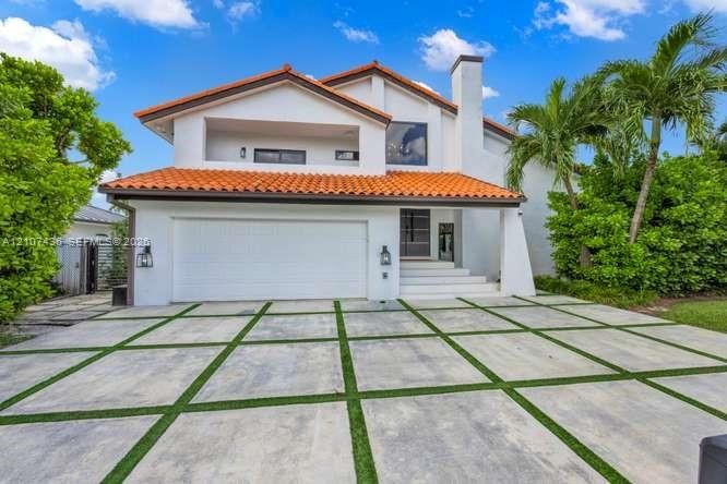 Two-story stucco exterior featuring a terracotta tile roof, second-story balcony, chimney stack, and expansive concrete paver driveway with turf accents
