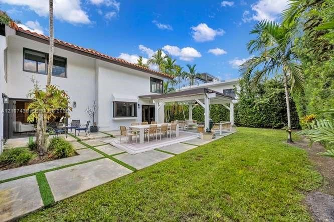 Outdoor living space featuring a white stucco exterior, concrete paver patio with grass inlay, covered pergola, and mature landscaping