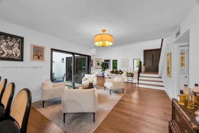 Spacious living area featuring wood-finish flooring, a drum shade pendant light, sliding glass doors, and a decorative staircase with wood treads