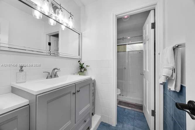 Grey vanity with white countertop, integrated sink, polished metal faucet, multi-bulb vanity light, and white tiled wall surround