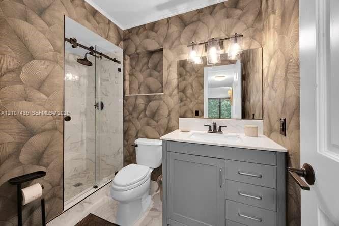 Bathroom featuring a gray vanity with a white countertop, glass-enclosed shower with sliding hardware, patterned wall covering, built-in shower niche, and three-light wall-mounted fixture
