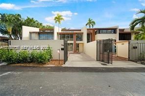 Modern stucco exterior featuring clean architectural lines, a gated paved driveway, and custom metal privacy fencing