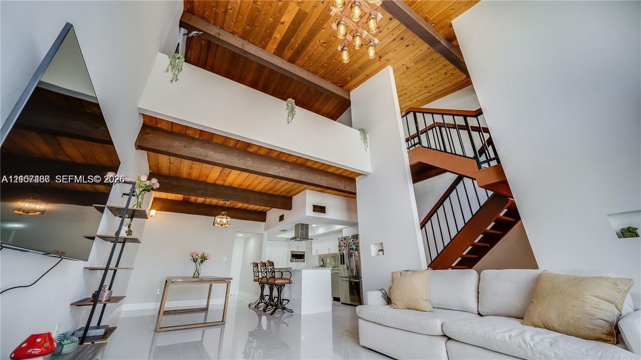 Vaulted ceilings with exposed timber beams, wood-plank ceiling finish, industrial-style staircase with metal railings, and polished tile flooring