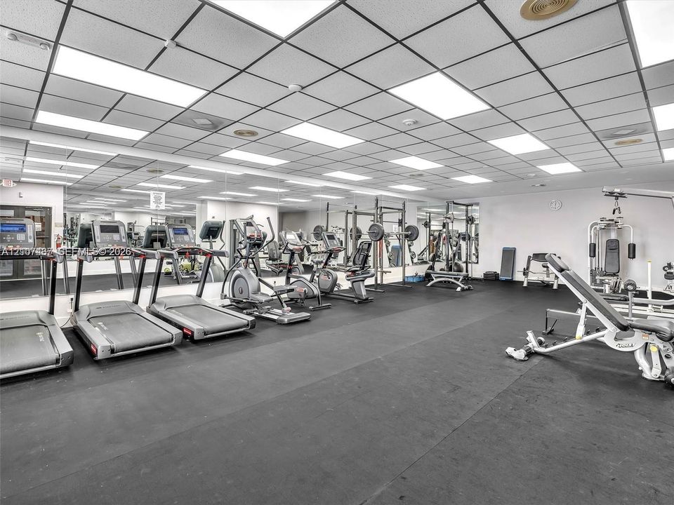 Fitness room featuring rubberized flooring, a drop ceiling with integrated fluorescent lighting, and wall-to-wall mirrors