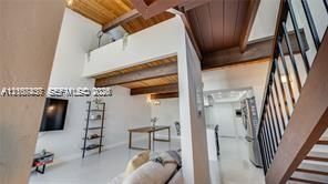 Vaulted ceilings featuring exposed wood beams, lofted mezzanine level, staircase with metal railings, and wood-finish ceiling accents