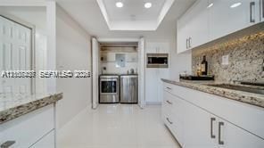 Kitchen featuring high-gloss white cabinetry, stone-finish countertops, recessed ceiling lighting, and a dedicated laundry area with stainless steel appliances