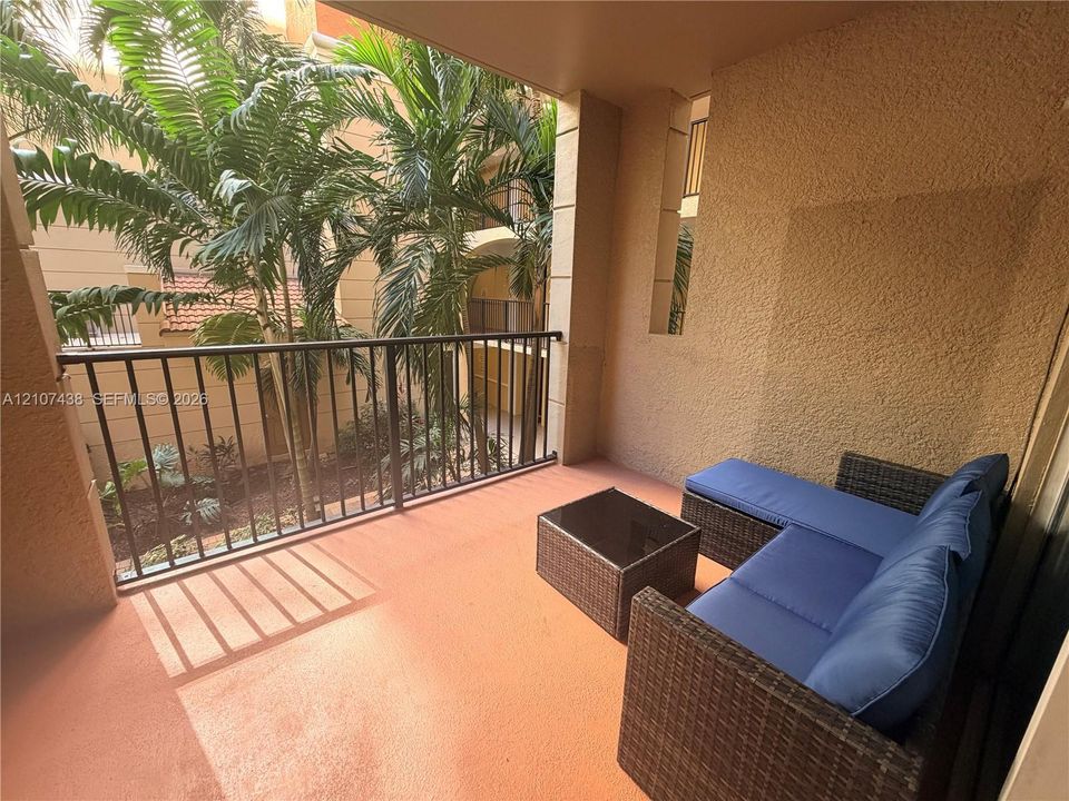 Covered balcony featuring textured stucco walls, a black metal railing, and concrete flooring