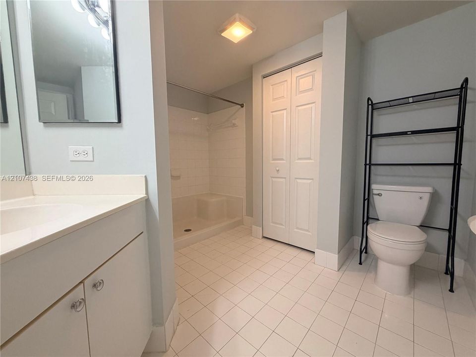 Bathroom featuring a white-finish vanity, a walk-in shower with tile surround, white floor tiling, and a bi-fold closet