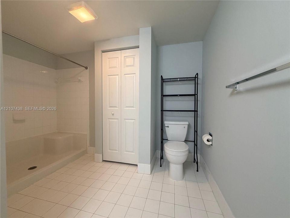 Bathroom featuring a walk-in shower with integrated seating, white tile flooring, bi-fold closet doors, and a porcelain toilet