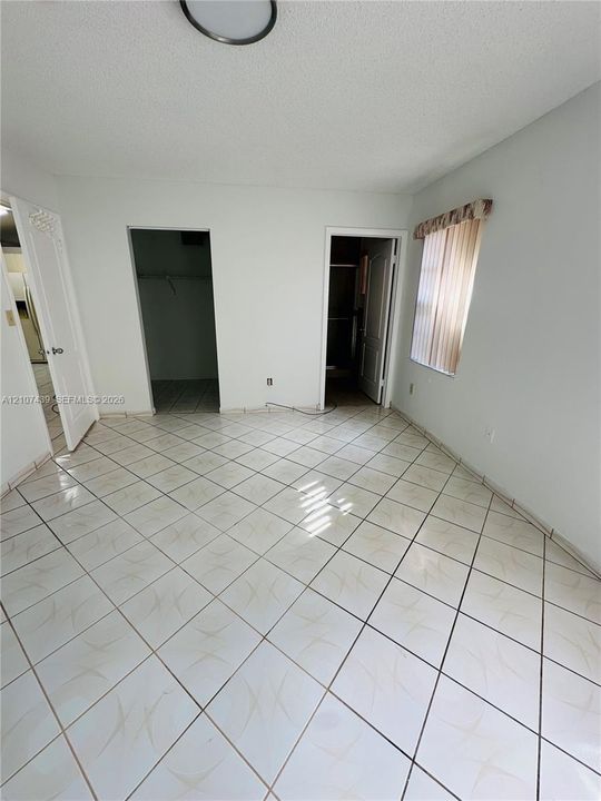 Interior space featuring diagonally laid tile flooring, two walk-in closet entries, and a window with vertical blinds