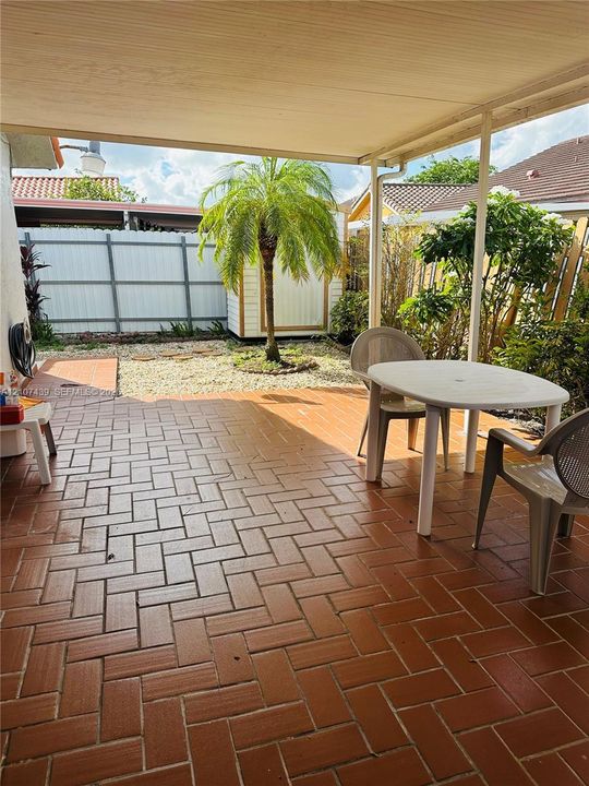 Covered patio featuring herringbone-patterned brick pavers, enclosed backyard, and privacy fencing