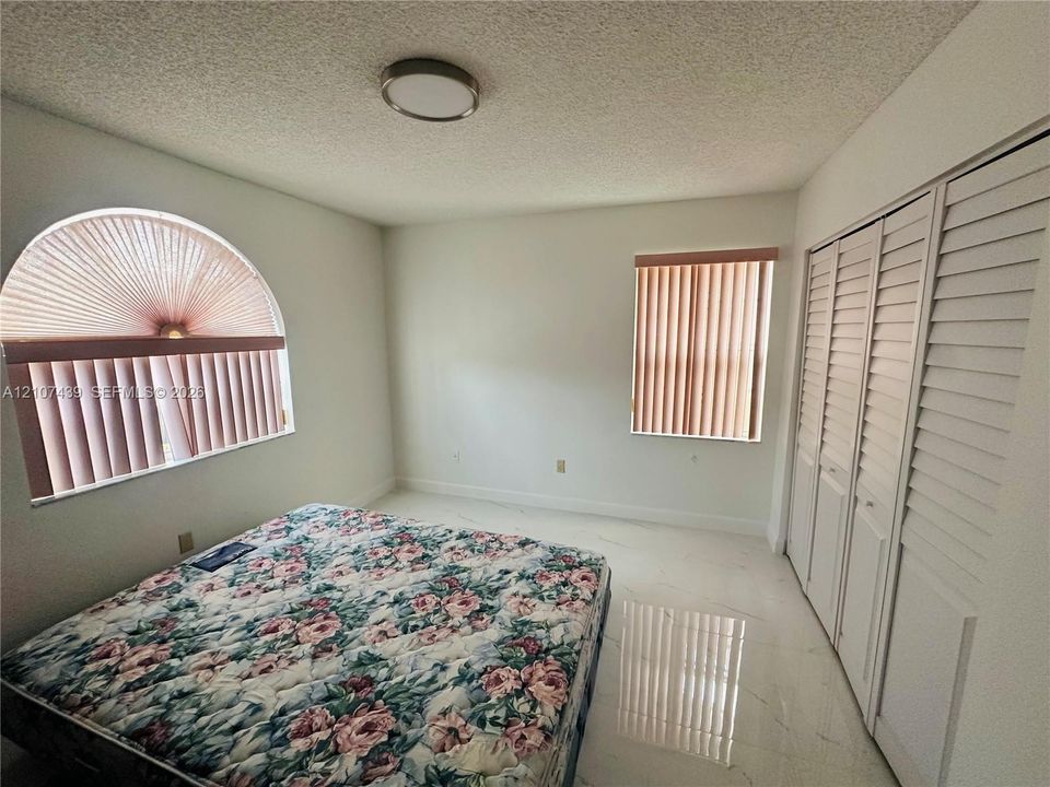 Arch-top window, rectangular window with vertical blinds, tile flooring, and floor-to-ceiling closet with louvered doors