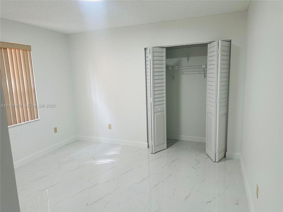 Interior room featuring white tile flooring with veining, a closet with white louvered bi-fold doors, a wire shelving system, and vertical window blinds