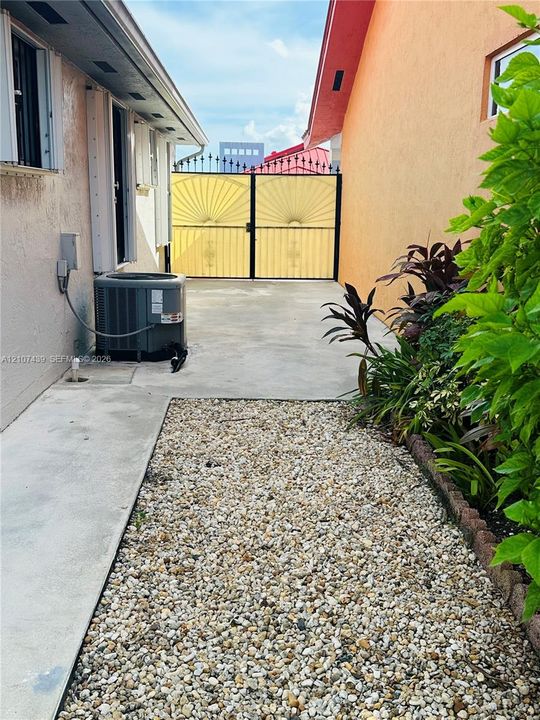 Exterior side yard featuring a concrete pad, decorative gravel landscape, and a wrought iron privacy gate