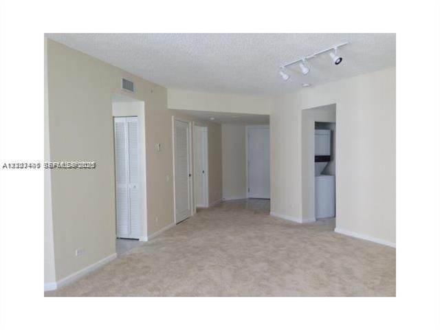 Interior space featuring neutral wall tones, wall-to-wall carpeting, overhead track lighting, louvered closet doors, and a built-in laundry area