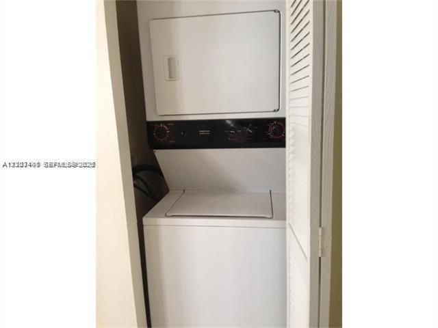 Stacked laundry center featuring a white top-load washer and front-load dryer enclosed by louvered bi-fold doors