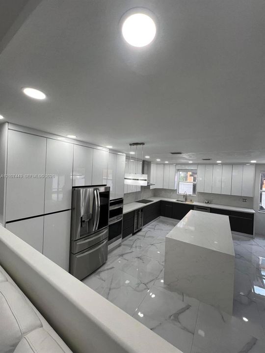 Open-concept interior featuring large-format polished tile flooring, white cabinetry with integrated hardware, recessed lighting, and a breakfast bar
