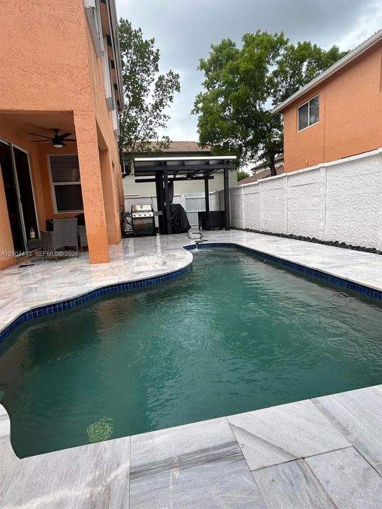 Stucco exterior residence featuring an in-ground pool, stone-paver patio, covered porch, and white vinyl privacy fencing
