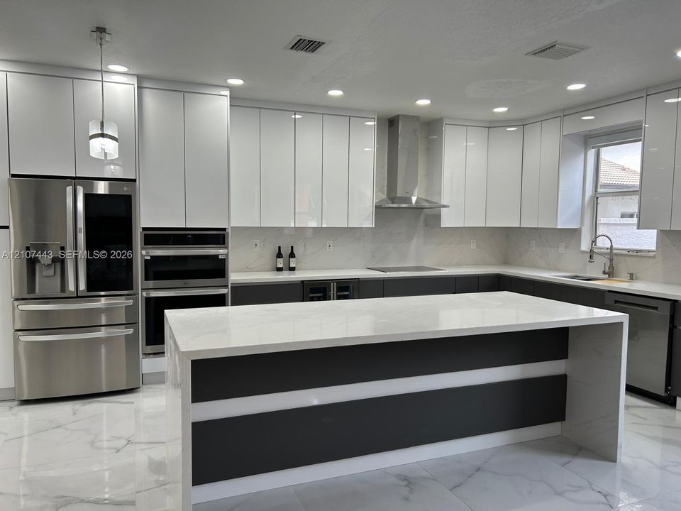 Kitchen featuring two-tone flat-panel cabinetry, a central island with stone-finish countertops, large-format tile flooring, stainless steel range hood, and recessed lighting