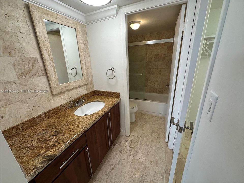 Bathroom featuring a vanity with wood-finish cabinetry, stone countertop with an undermount sink, matching stone-tiled walls, and a separate tub and shower enclosure with a glass door