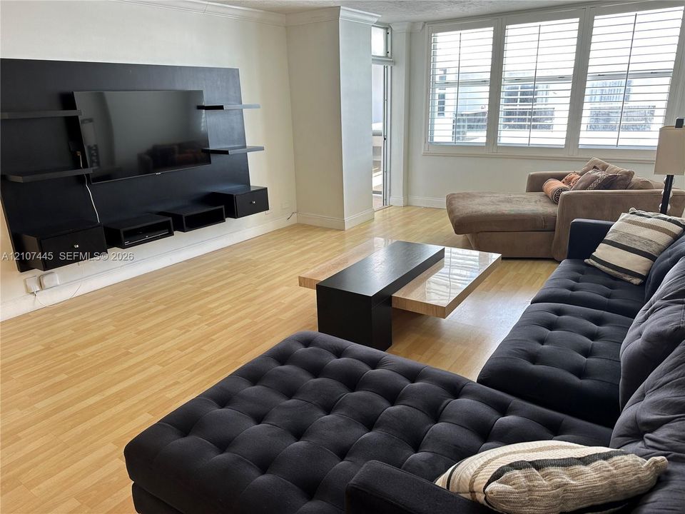 Living area featuring wood-finish flooring, white wall trim, and a custom built-in black media unit with shelving and drawers
