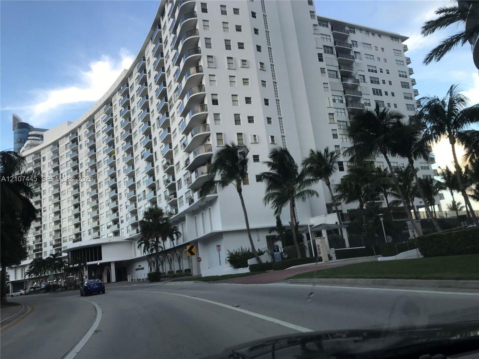 High-rise multi-story building featuring curved architectural lines, exterior glass-railed balconies, and surrounding palm tree landscaping