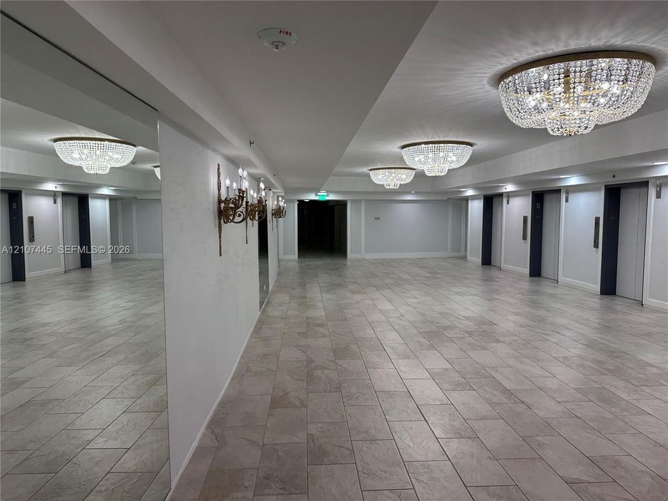 Expansive lobby area featuring neutral tile flooring, floor-to-ceiling mirror paneling, tiered crystal flush-mount chandeliers, and decorative wall-mounted candelabra-style light fixtures