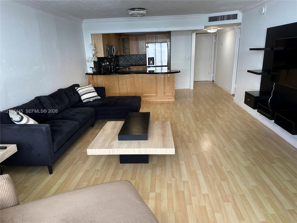 Living area featuring wood-finish flooring and built-in wall shelving, paired with a kitchen peninsula, stone countertops, and stainless steel appliances