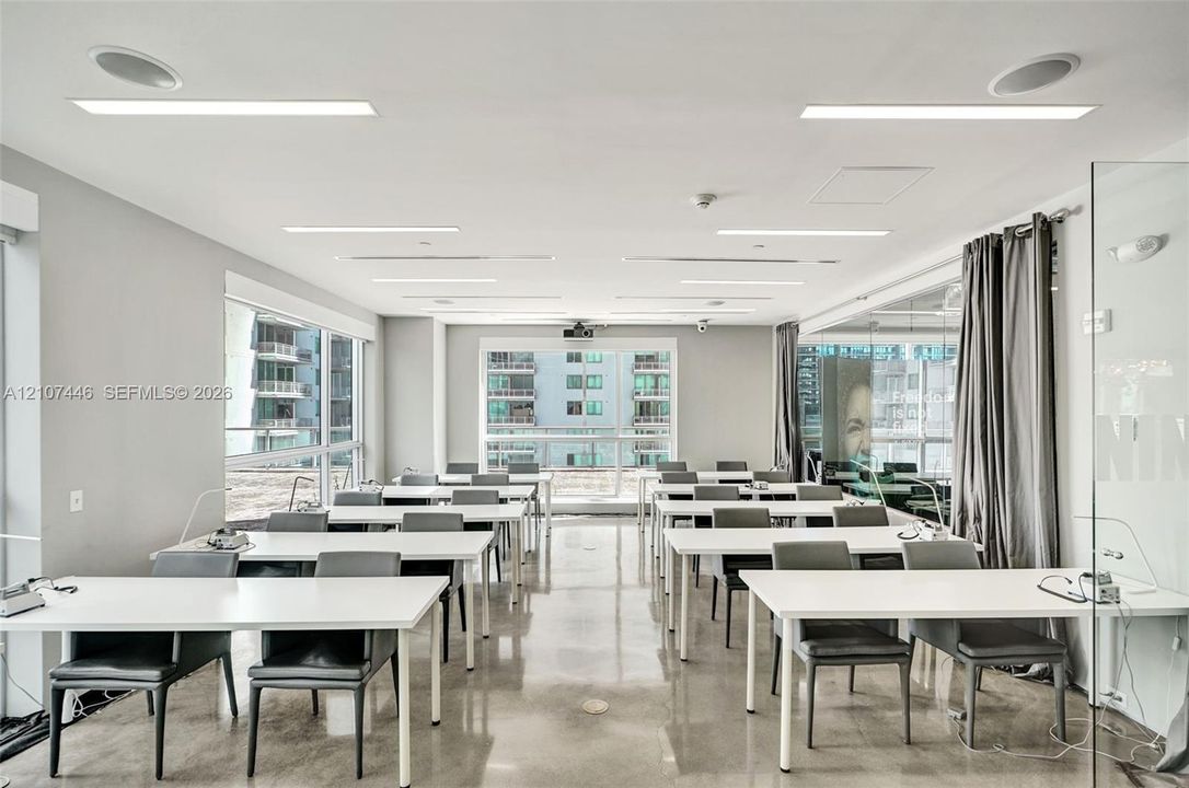 Expansive room featuring polished concrete flooring, recessed linear lighting, integrated ceiling speakers, floor-to-ceiling windows, and glass partition walls