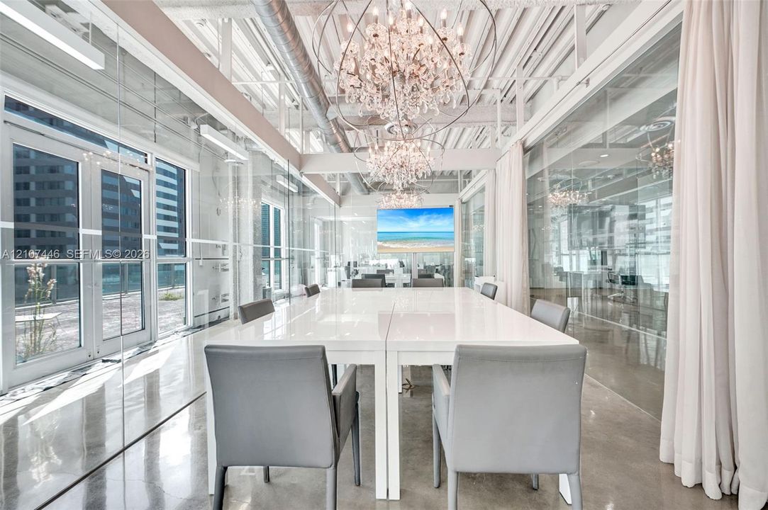 Exposed industrial ceiling with ductwork, expansive glass wall partitions, polished concrete flooring, multiple crystal chandeliers, and exterior glass door access