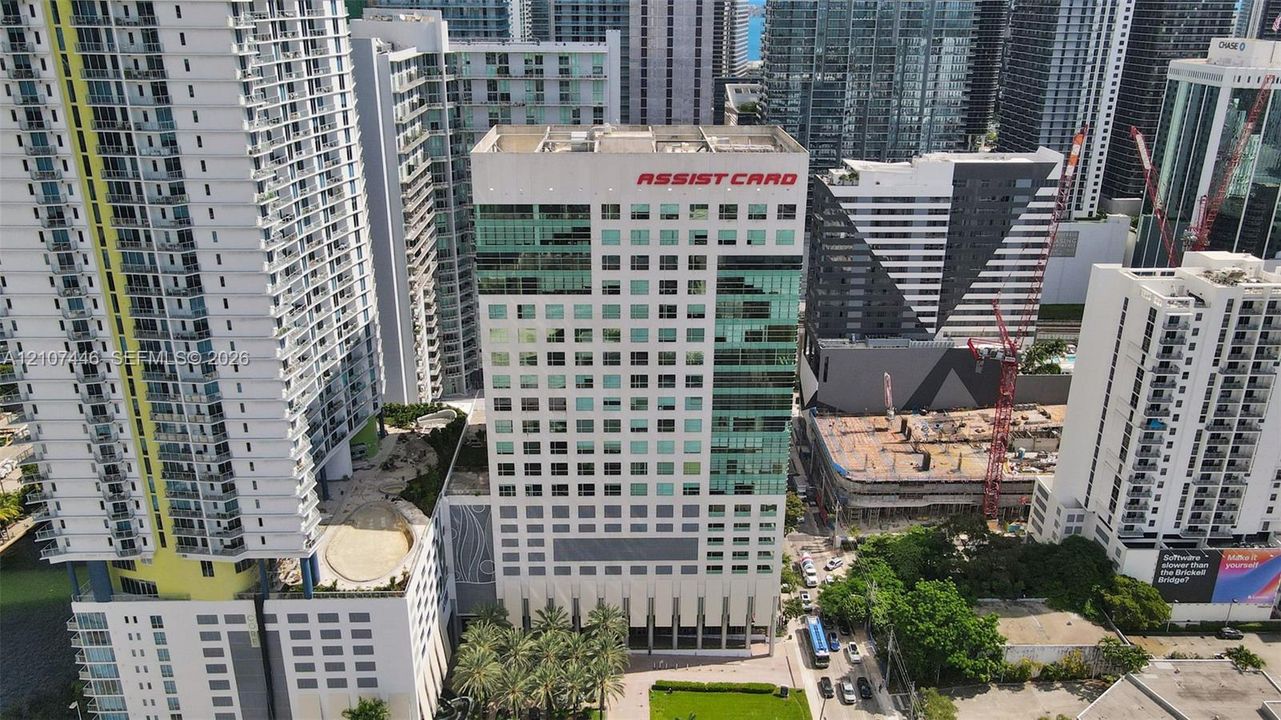 High-rise commercial building featuring a multi-story glass curtain wall, reinforced concrete facade, ground-level professional landscaping, and palm-lined street frontage in a dense urban setting