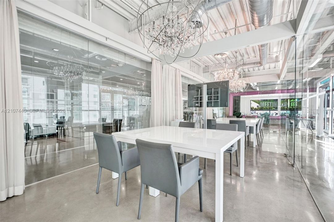 Open-concept interior featuring polished concrete flooring, exposed overhead industrial ductwork, floor-to-ceiling glass wall partitions, and decorative crystal-style chandeliers