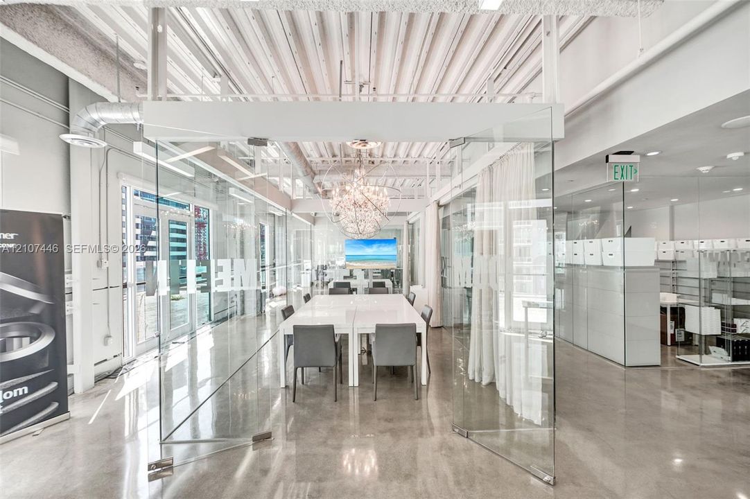 Industrial-style interior featuring high vaulted ceilings with exposed beams, polished concrete flooring, glass-paneled walls, and a large decorative crystal chandelier