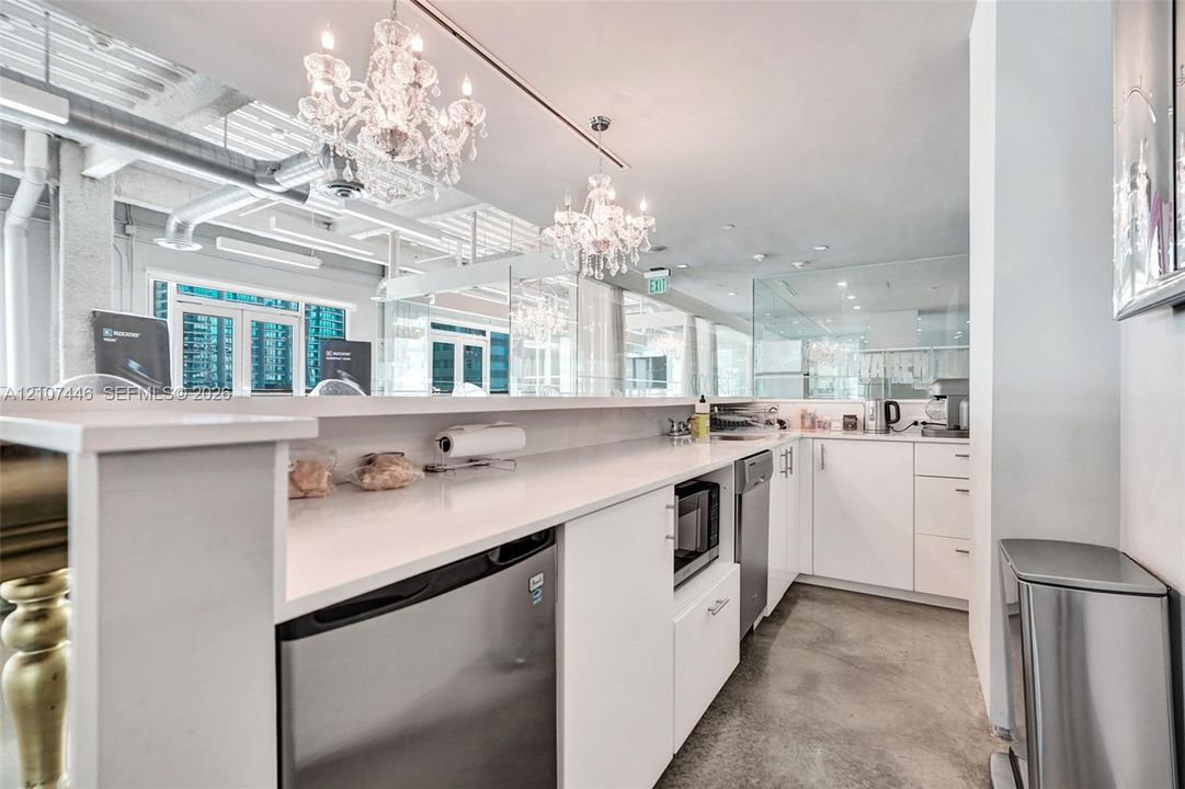 Kitchen area featuring white cabinetry, solid-surface countertops, industrial-style exposed ductwork, polished concrete flooring, and crystal chandelier lighting fixtures