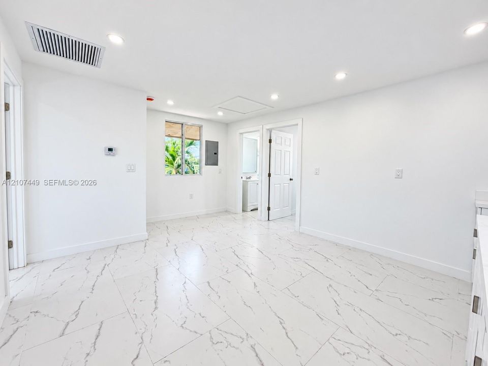 Large-format white tile flooring with grey veining, recessed lighting, and white paneled doors