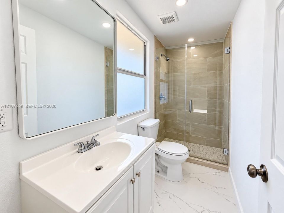 Bathroom featuring a vanity with integrated sink, rectangular mirror with rounded corners, walk-in shower with glass enclosure, beige wall tile, and stone-finish flooring
