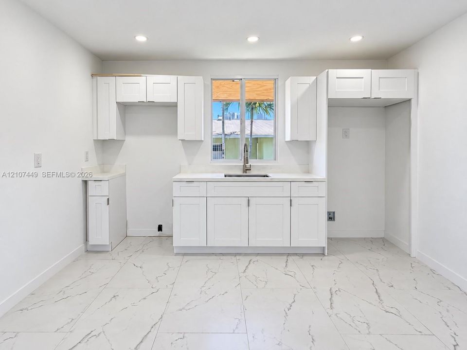 Kitchen featuring white Shaker-style cabinetry, solid-surface countertops, integrated stainless steel sink with pull-down faucet, recessed lighting, and large-format tile flooring