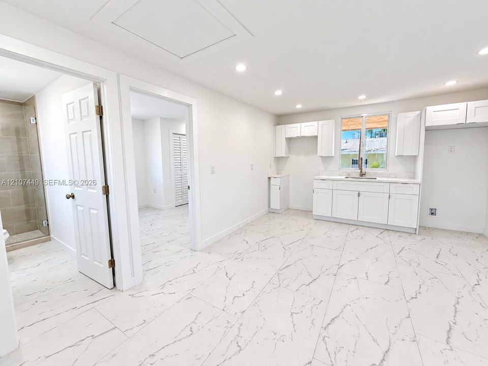Kitchen featuring white shaker-style cabinetry, stone-patterned tile flooring, recessed ceiling lighting, and a walk-in shower with neutral tile surround