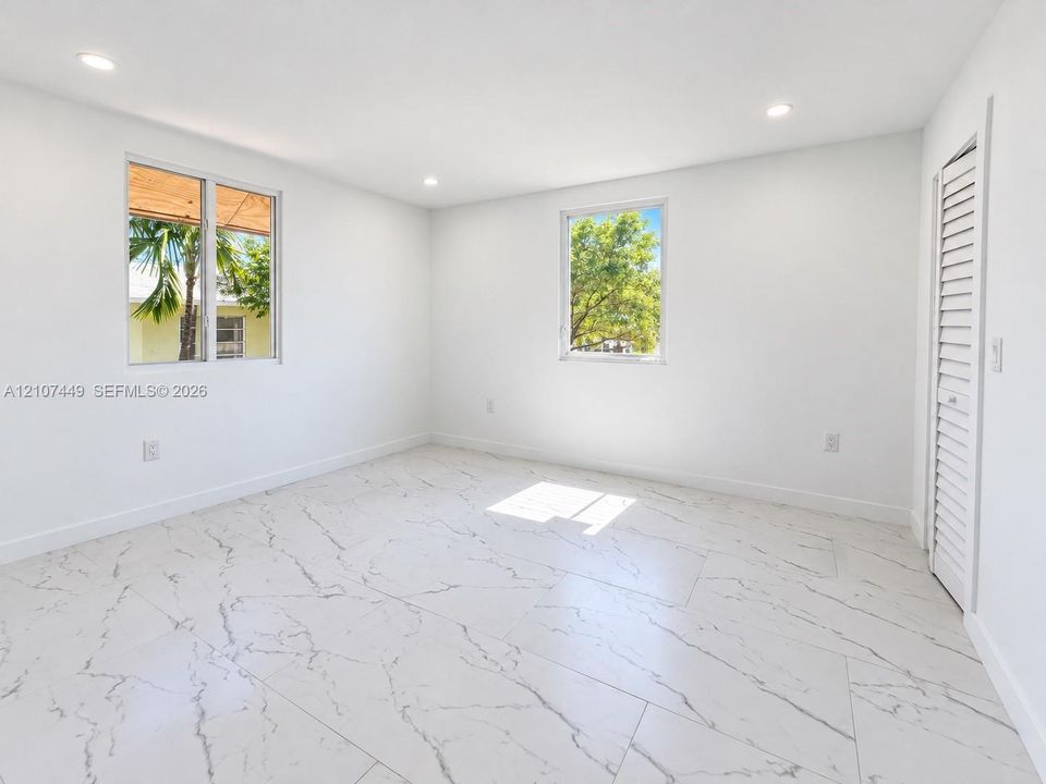 Neutral interior room featuring large-format tile flooring with a veined pattern, recessed lighting, and white louvered closet doors