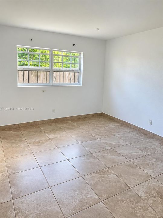 Interior room featuring large-format neutral tile flooring, expansive wall surfaces, and a multi-pane sliding window