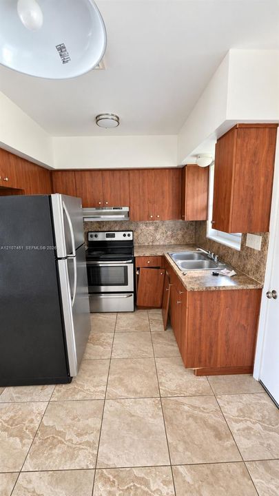 Kitchen featuring wood-finish cabinetry, stone-pattern laminate countertops, stainless steel range and refrigerator, dual-basin stainless steel sink, and ceramic tile flooring
