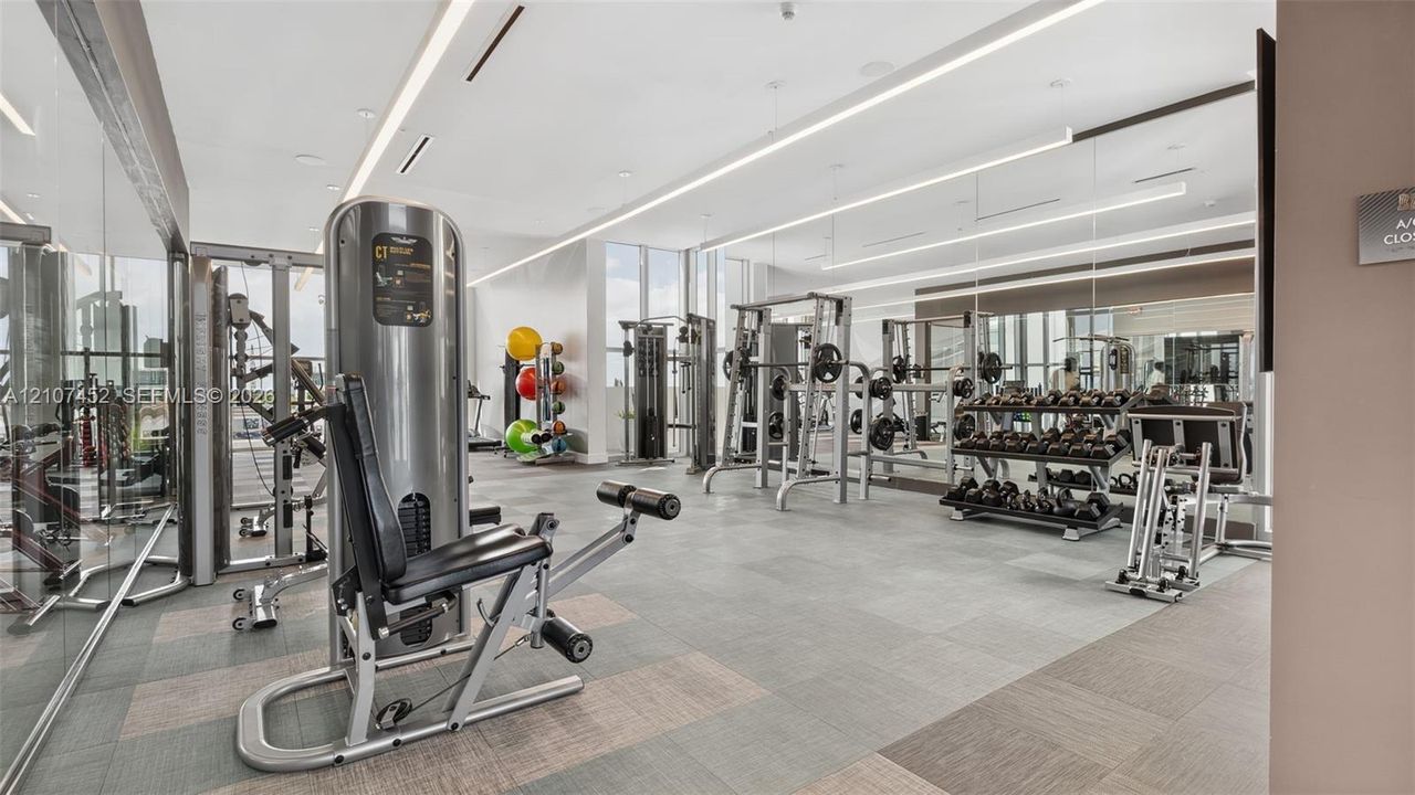 Fitness center featuring wall-to-wall mirrors, recessed linear lighting, floor-to-ceiling windows, and integrated strength training equipment