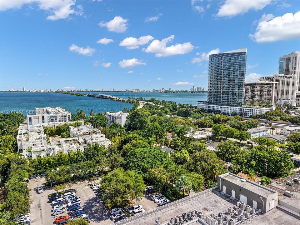 Aerial perspective featuring coastal water, a bridge, metropolitan high-rise buildings, and dense tropical landscaping