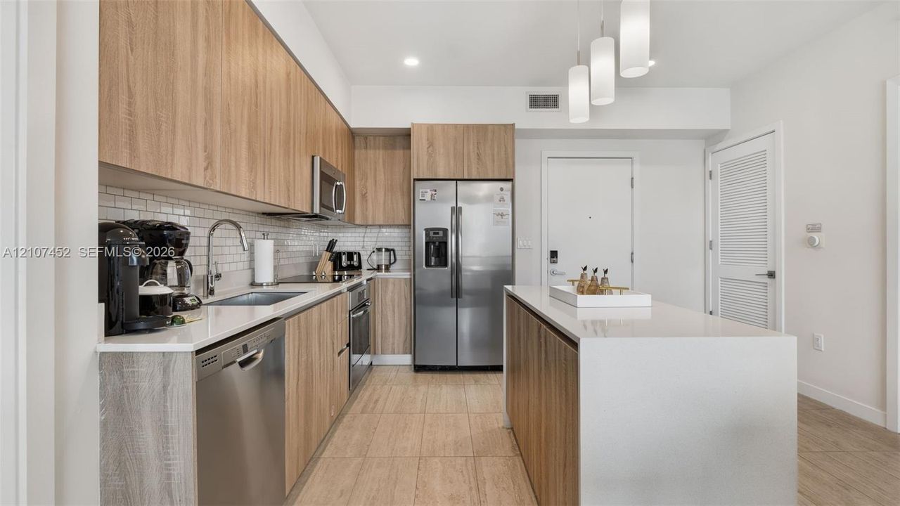 Kitchen featuring wood-finish cabinetry, stone-style countertops, stainless steel appliances, subway tile backsplash, and a central island with pendant lighting