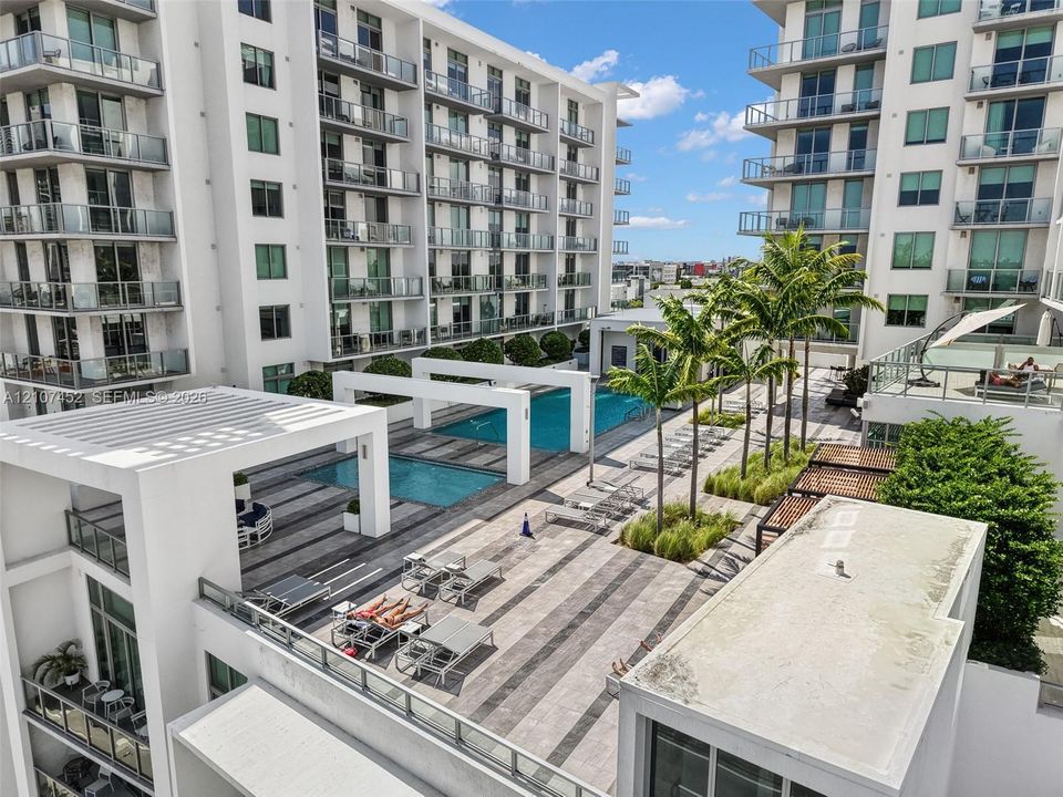 Swimming pool terrace featuring large-format paver tile decking, pergola structures, integrated landscaping, and glass-paneled balconies