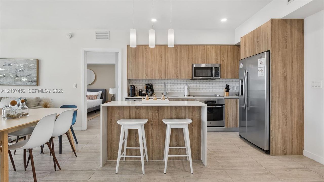 Kitchen featuring wood-finish cabinetry, a waterfall-edge island, subway tile backsplash, stainless steel appliances, and pendant lighting